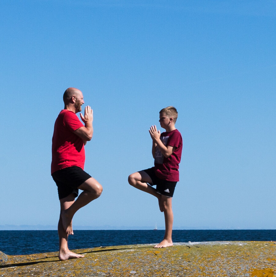 En man och en pojke som gör yoga på en klippa